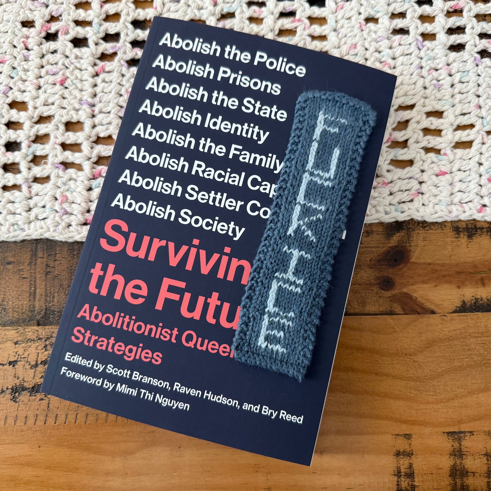 Book titled 'Surviving the Future: Abolitionist Queer Strategies' with a woven mat and wooden surface in the background.